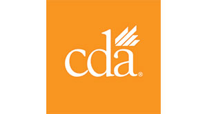 The image shows a logo with text that reads  CDA  and includes an emblem resembling a stylized crown, set against a backdrop of two shades of orange, one lighter than the other, with a small portion of gray visible at the bottom left corner.