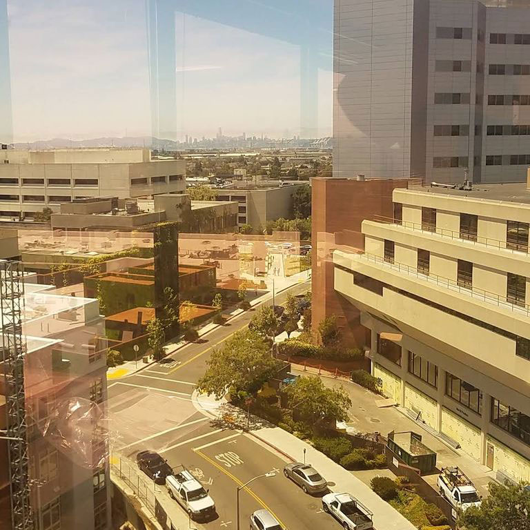The image shows an urban view from a high vantage point, featuring a city skyline with buildings, roads, and parking lots.