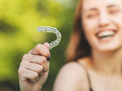 A smiling woman holds up a clear plastic dental retainer.