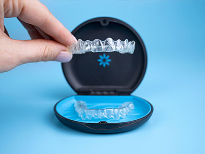 An individual s hand holding an open plastic case containing a clear dental retainer.