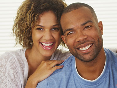 A man and woman smiling at the camera, posing together for a photograph with a warm and happy demeanor.