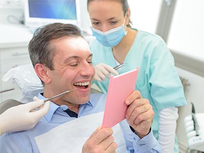 A man sitting in a dentist s chair, holding up a piece of paper with a smile, while a dental professional looks on.