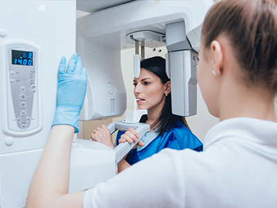 A woman in a blue jacket stands next to a large white machine with digital readouts while another person looks on, both are in a room with medical equipment and a clean, professional atmosphere.