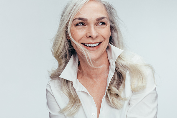 Woman with gray hair smiling at camera, wearing a white top.